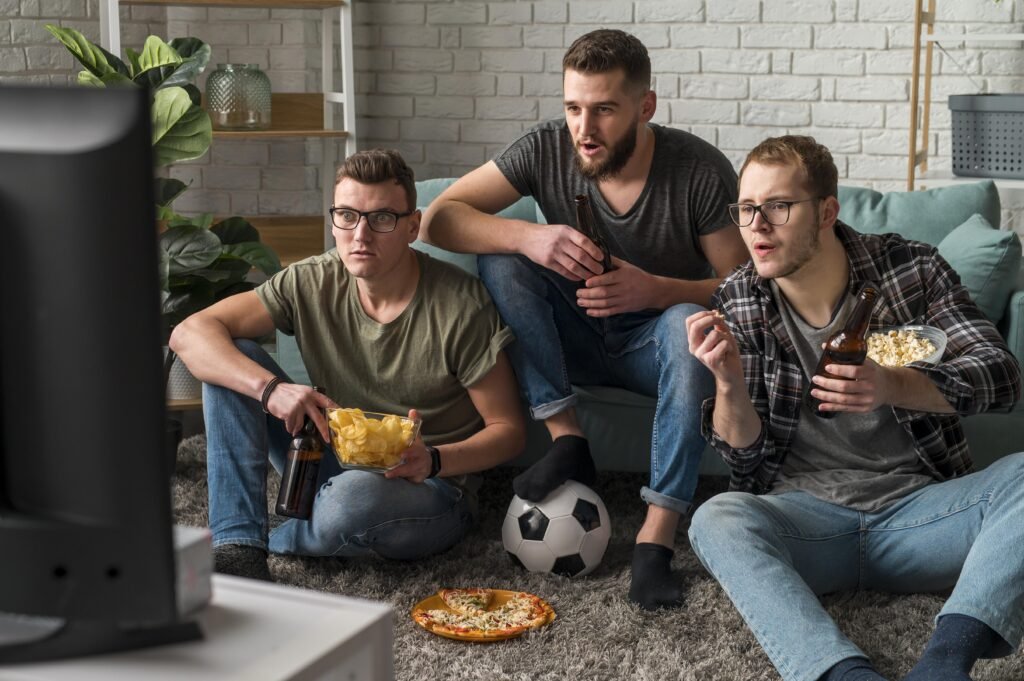front view three male friends watching sports tv together while having snacks beer